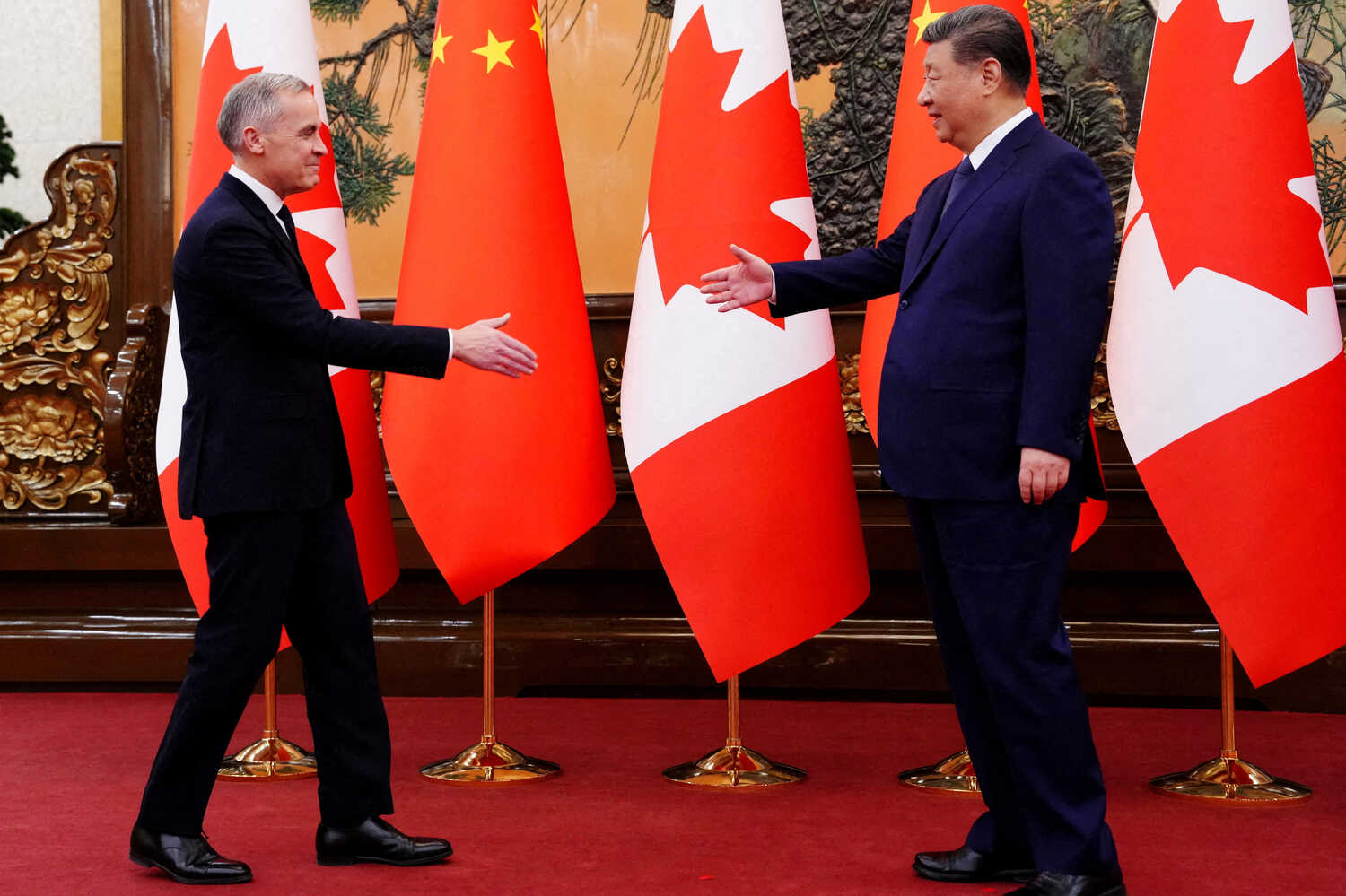Xi Jinping and Mark Carney meet, extending hands in greeting. They stand in front of red and white flags on a red carpet.