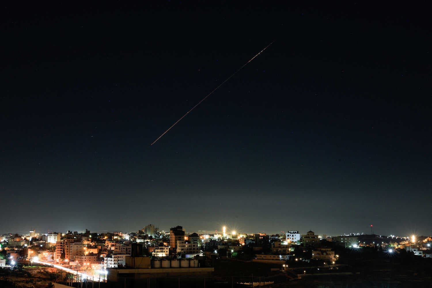 A streak of light of a projectile is seen above a city at night.