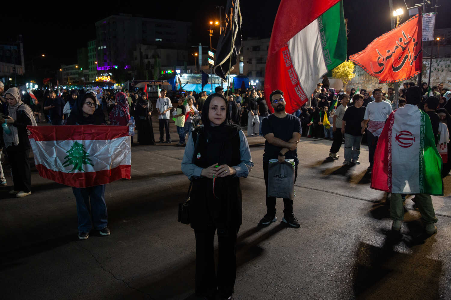 A large gathering of people on a city street at night. Some are carrying flags.